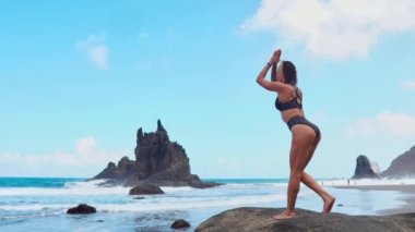 yoga poz lotus kayaların üzerinde çalışan okyanus dalgaları karşı mor mat siyah top sarışın kız rahatlatır