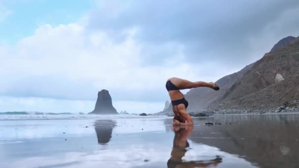 Mujer de yoga flexible que se estira hacia adelante dobla tocando la frente hasta las rodillas al aire libre al atardecer playa de mar de cerca. Instructor de fitness gimnasta profesional realiza asana Uttanasana de pie descalzo sobre la arena . — Vídeo de stock