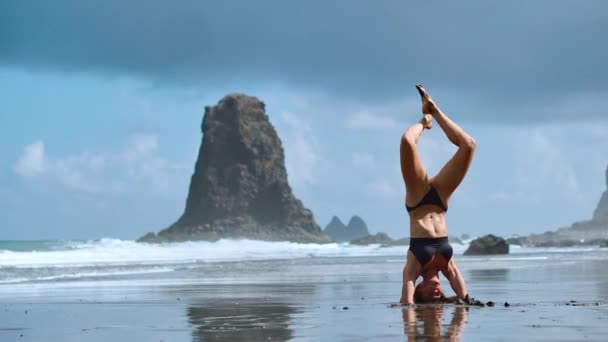 Sesión de yoga al amanecer de verano en la hermosa playa de La Tejita con vista al océano atlántico y la roca Punta Roja - isla tropical de Tenerife, Canarias en España. Cabezal apoyado, Salamba Sirsasana — Vídeos de Stock