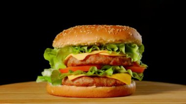 Siyah arka plan üzerine ahşap bir gemide büyük hamburger biftek pirzola, domates, mantar ve salatalık eritilmiş peynir ile döner.