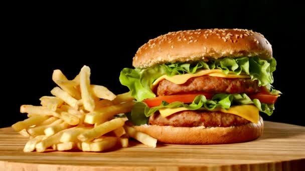 Hamburguesa artesanal de res y papas fritas sobre mesa de madera aislada sobre fondo negro . — Vídeo de stock