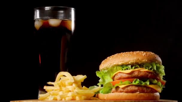 Hamburguesa con papas fritas y un vaso con cola de hielo sobre un fondo rústico negro — Vídeo de stock