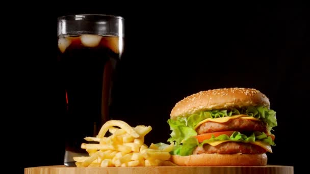 Hambúrguer com batatas fritas e um copo com cola de gelo em um fundo rústico preto — Vídeo de Stock