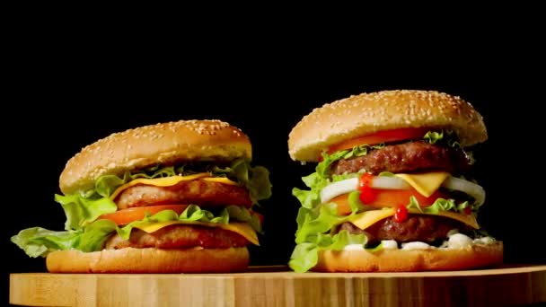 Twee ambachtelijke rundvlees hamburgers op houten tafel geïsoleerd op donkere grijstinten achtergrond. — Stockvideo