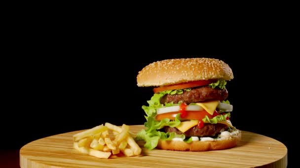 Hamburguesa artesanal de res y papas fritas sobre mesa de madera aislada sobre fondo negro . — Vídeos de Stock