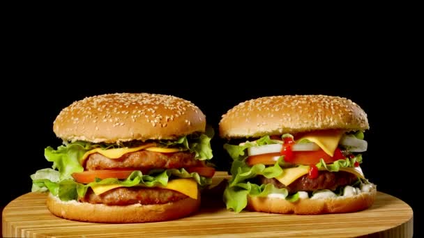 Dos hamburguesas artesanales de ternera sobre mesa de madera aisladas sobre fondo en escala de grises oscuros . — Vídeo de stock