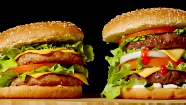 The concept of American fast food. Juicy American burger with two beef cutlets, with sauce and ogretsami on a black background. Copy space — Stock Video