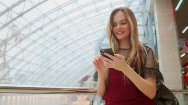 Dívka používat mobilní telefon, Rozostřit obraz uvnitř obchoďáku jako pozadí. — Stock video