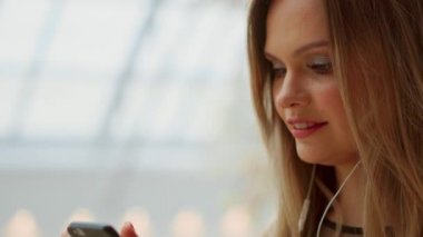 Sırt çantası ile şapka kadında genç turist havaalanında standları ve smartphone kullanır. Hippi kız e-posta, sohbet, bloglama, internet tarama denetler. Online pazarlama, eğitim. Mesafe iş, e-öğrenme.