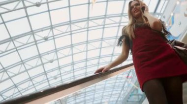 Güzel bir kız yürüyen merdiven iner, Alışveriş yılında telefon konuşması.