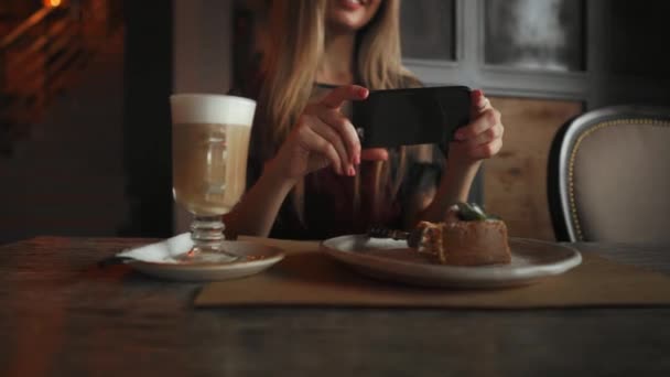 美しい感情的な幸せな女の子がカフェ、テーブル、デザート アイス クリーム チョコレート桜ケーキ ミント、ソーシャル ネットワークでのコミュニケーションにラテで食べ物の写真を作っています。 — ストック動画