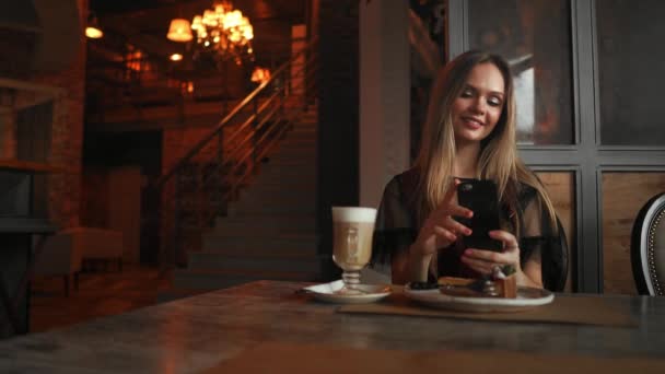 Hermosa chica feliz emocional está haciendo foto de la comida en la cafetería, café con leche en la mesa, postre helado pastel de chocolate menta cereza, comunicación en las redes sociales — Vídeos de Stock