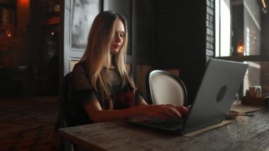 Yan görünümü. Tablo ve not defterindeki not almak oturan genç iş kadını. Masada dizüstü bilgisayar, akıllı telefon ve kahve var. Bilgisayar ekran grafikleri ve çizelgeleri üzerinde. Öğrenci öğrenme online. Blogger.