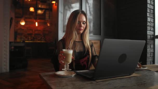 Vista lateral. Joven mujer de negocios sentada en la mesa y tomando notas en el cuaderno. En la mesa está el portátil, el teléfono inteligente y la taza de café. Aprendizaje de estudiantes online. Blogger . — Vídeo de stock