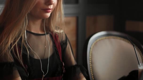 Молода красива жінка в окулярах працює в кафе, слухаючи музику і посміхаючись . — стокове відео