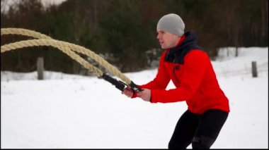 Genç kaslı adam kırmızı ceket eğitim Savaşı ile kış ve kar, ağır çekim ipleri. Fitness Egzersiz açık havada.