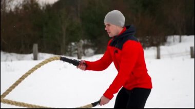 Genç kaslı adam kırmızı ceket eğitim Savaşı ile kış ve kar yavaş hareket ipleri. Fitness Egzersiz açık havada.