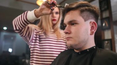 Modern berber dükkanı çalışma sürecinde iç vurdu. Yan görünümü son moda saç kesimi almak çekici genç adam portresi. Erkek kuaför hizmet istemci, metal makas ve tarak kullanarak saç kesimi yapma.