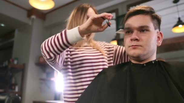 Plan intérieur du processus de travail dans le salon de coiffure moderne. Vue de côté portrait de jeune homme attrayant obtenir coupe de cheveux à la mode. Coiffeur masculin servant le client, faire une coupe de cheveux à l'aide de ciseaux en métal et peigne . — Video