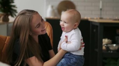 Anne Bebek ve çocuk gülümsüyor sevgili annesine bakarak sarılmak. Birlikte beyaz mutfakta Noel arifesinde çelenk ve Noel ağaçları arka plan üzerinde bekletin. Mutlu anne ve bebek