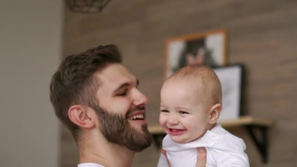 Люблячий батько в білій футболці обіймає дитину і цілує дитину сміється і посміхається на тлі ялинки і гірлянди — стокове відео
