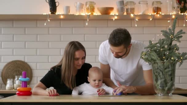 Concepto de familia, paternidad y personas: madre y padre felices mostrando la computadora de la tableta al bebé en casa — Vídeo de stock