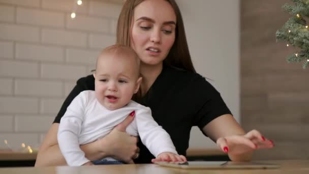 Mamá y el bebé sentado en la mesa jugando tableta de computadora presionando los dedos en la pantalla y riendo — Vídeos de Stock
