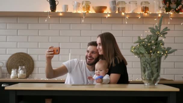 Familie, ouderschap en mensen concept - gelukkige moeder en vader met baby nemen selfie thuis — Stockvideo