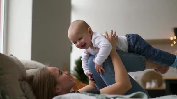 Concepto de familia, maternidad y personas - madre feliz besando al pequeño bebé durante las fiestas luces de fondo — Vídeo de stock