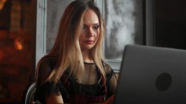 Ahşap masa kahve dükkanında otururken, kahve içme ve smartphone kullanarak genç kadın. Masada dizüstü bilgisayardır. Kız sohbet, internet, bloglama tarama. Kadın telefon tutarak ve onun ekranda arıyor.
