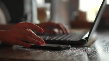 Yakın çekim dikiz ofis iç akıllı telefon tutarak ve diyagramları ile ekrana bakarak pc üzerinde çalışan genç iş kadını. Cep telefonu ve dizüstü bilgisayar kullanan office kişi.