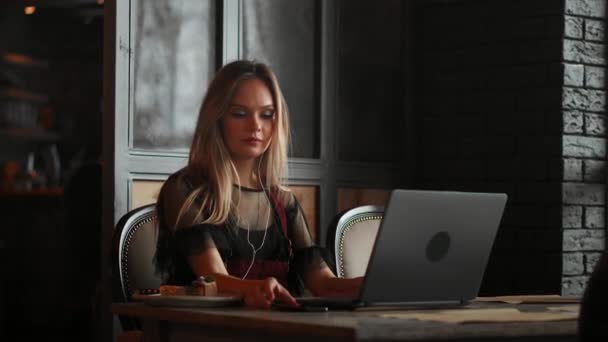 Jeune femme assise dans un café à une table en bois, buvant du café et utilisant un smartphone. Fille naviguant sur Internet, bavardant, bloguant. Femme tenant téléphone et regardant sur son écran . — Video