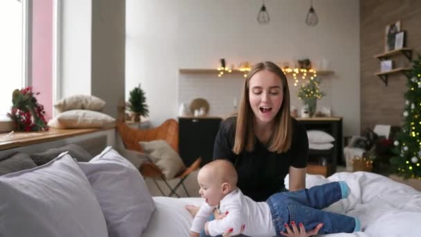 Vamos a volar alegre hermosa mujer joven sosteniendo a la niña en sus manos y mirándola con amor mientras está sentada en el sofá en casa — Vídeos de Stock