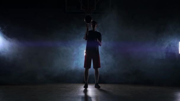 Basketballspieler, der in einer dunklen Sporthalle mit Rauch verschiedene Tricks vorführt und Ball dreht. Zeitlupe — Stockvideo