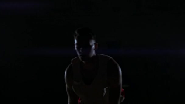 Samec urban basketbalista kapky míč ve skrčené v městské košíkovou osvětlena jediné pouliční lampy — Stock video