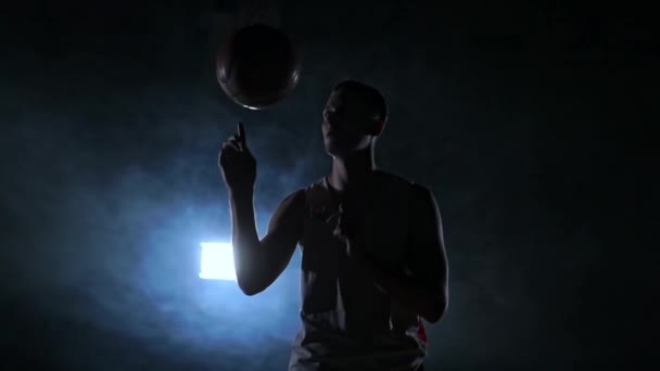 Крупним планом кадри баскетболіста обертається м'яч на пальці, темна туманна кімната з прожектором — стокове відео