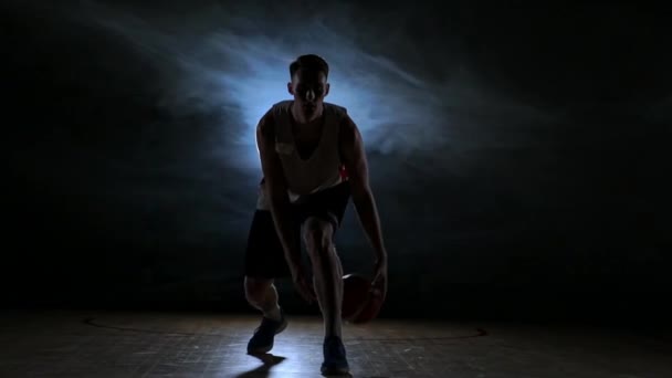 Um jovem adulto, jogador de basquetebol, bola de drible, campo de basquetebol escuro dentro de casa. Movimento lento — Vídeo de Stock