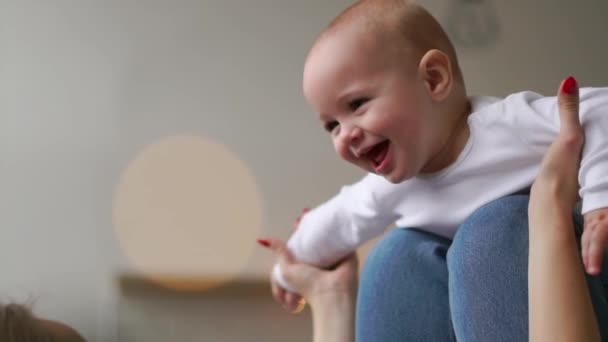 En baby i en vit t-shirt ligger på hans mödrar knä imitera flygningen av flygplan — Stockvideo