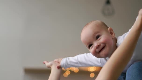 Madre juega con el bebé en una camiseta blanca acostado en la cama, un niño vuela y se ríe — Vídeos de Stock