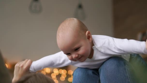 Mama spielt mit Baby in weißem Tank-Top auf dem Bett liegend, Baby fliegt und lacht. Zeitraffer des Zusammenspiels von Mutter und Kind. Flugsimulation — Stockvideo