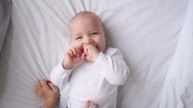Bebek beyaz bir yatakta yatarken ve kamera yukarıdan yavaş hareket seyir gülüyor beyaz t-shirt