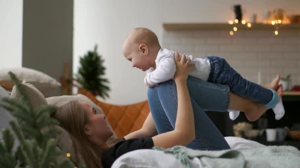 Mamma leker med Baby i vitt linne ligger på sängen, baby flyger och skrattar. Tidsfördröjning för av spelar tillsammans mor och barn. Flygsimulering — Stockvideo