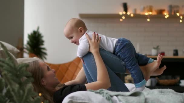 Mama spielt mit Baby in weißem Tank-Top auf dem Bett liegend, Baby fliegt und lacht. Zeitraffer des Zusammenspiels von Mutter und Kind. Flugsimulation — Stockvideo