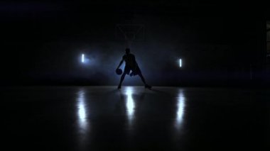 Bir basketbol basketbol halka duman zemin karşı bir karanlık basketbol sahası üzerinde bir adamla üç fenerler arka ışık tarafından aydınlatılmış top sürme becerileri gösterir
