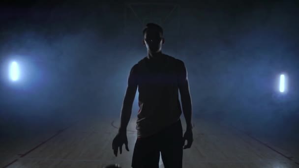 Basketball player goes straight to the camera in a dark room with a backlit back in the smoke looking at the camera in slow motion. Steadicam — Stock Video