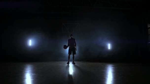 Мастерство дриблинга баскетболиста в темноте на баскетбольной площадке с подсветкой назад в дыму. Медленное движение стритбола — стоковое видео