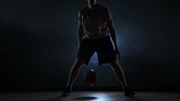 Basketbolcu duman yavaş çekimde bir arka ışık ile karanlık bir odada topu ile sahada top sürme — Stok video