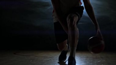Basketbolcu duman yavaş çekimde bir arka ışık ile karanlık bir odada topu ile sahada top sürme