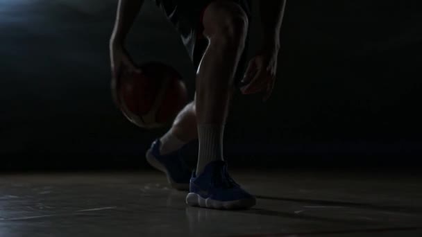 Дриблинг баскетболист крупным планом в темной комнате в дыму крупным планом в замедленной съемке — стоковое видео