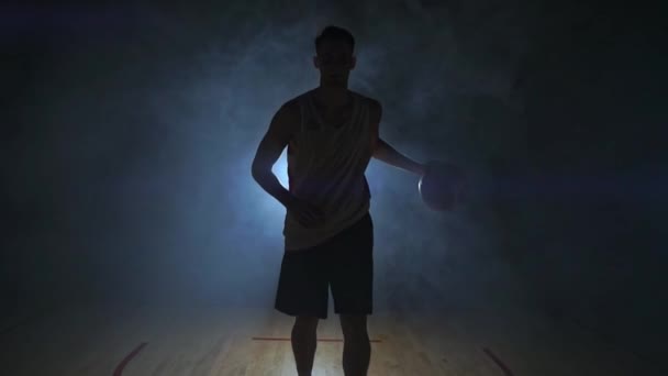Баскетболіст їде на камеру в темній кімнаті з підсвічуванням назад в диму, дивлячись на камеру в уповільненому Русі. Стедікам — стокове відео